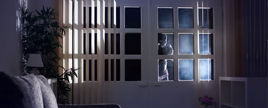 Burglar looking in window at night through vertical blinds