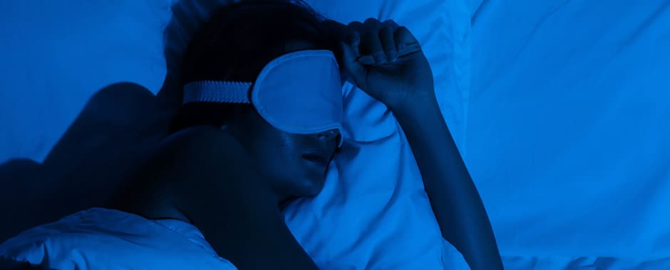 Woman asleep in pitch black room with eye mask on