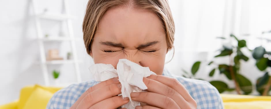 Woman sneezing into tissue due to allergy at home