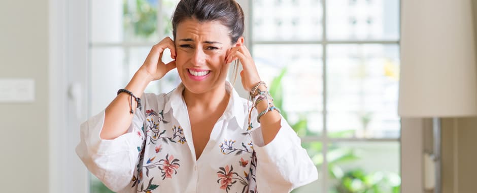 Woman at kitchen window covering ears with fingers due to noise