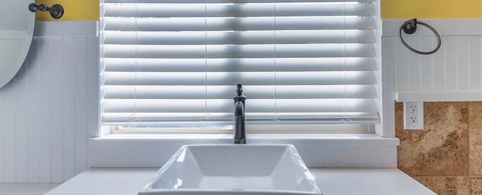 Partially closed white faux wood blinds at bathroom window