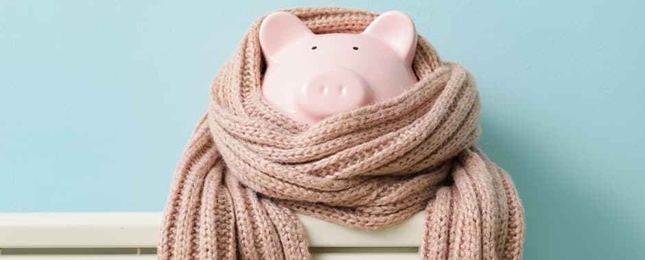 Pink piggy bank in scarf keeping warm on the radiator