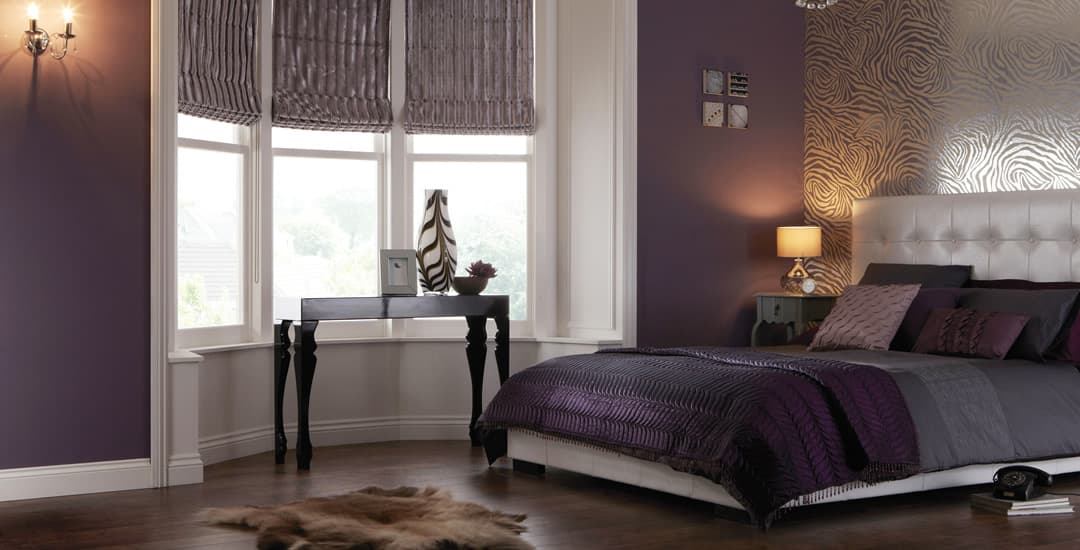 Purple velvet roman blinds in the bay window of a plush purple bedroom